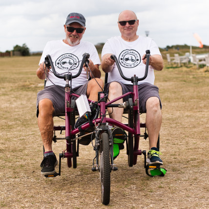 Two men on an adapted bicycle in a field.