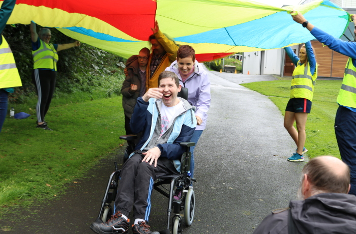 Disabled man and woman playing with a circle rainbow parachute. 