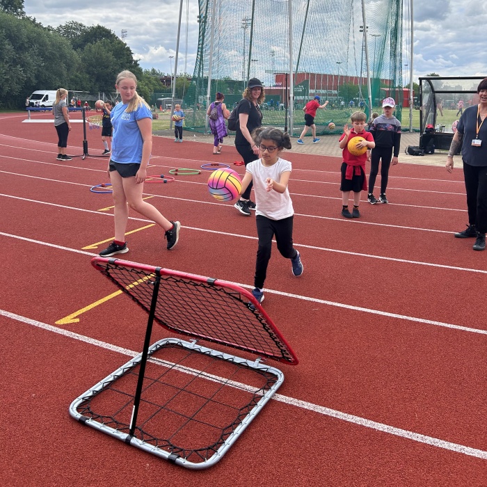 Young girl taking part in inclusive activity with a ball on an athletics track.  