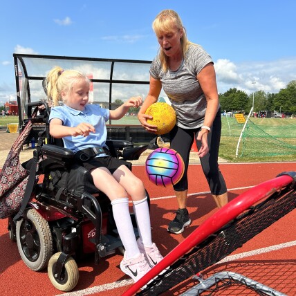 Disabled girl and woman playing with a net and a sports ball on an athletics track. 