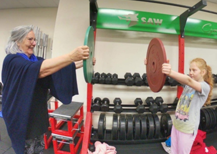 A grandmother and granddaughter holding out a weighted plate in front of them in a gym.