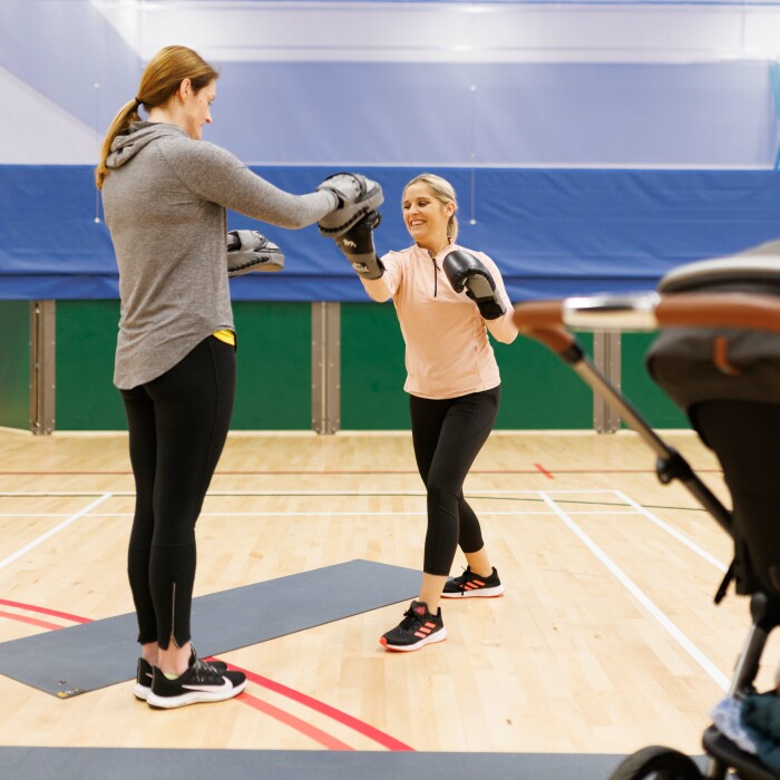 Two women wearing boxing gloves taking part in a buggy fit class. 
