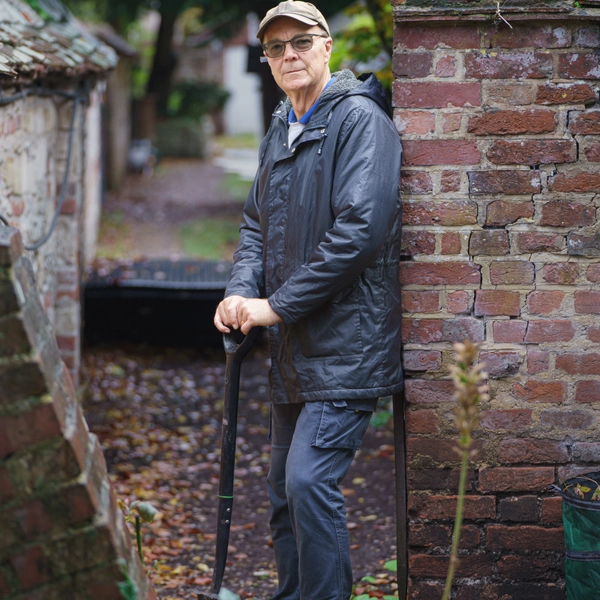 Andy stood with a spade leaning against a wall in a garden. 