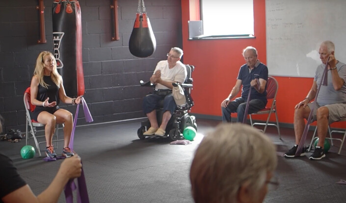 Group of disabled and non-disabled people sat in a circle in a boxing gym taking part in an exercise session.